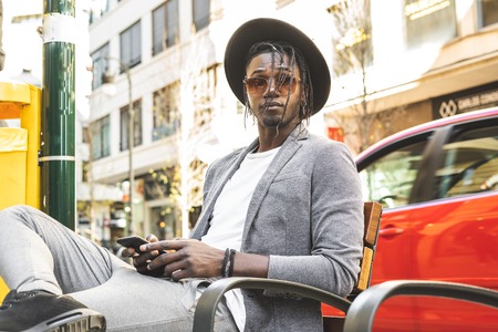 Portrait of modern African-American guy looking at the mobile phone on the street