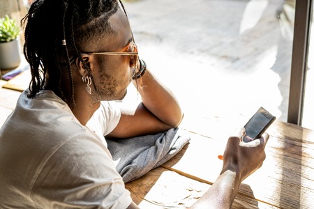Handsome african american portrait looking at a mobile phone in a coffee shopの写真素材