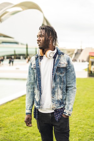 Outdoor portrait of a handsome young African smiling and with music headphones. Concept of...