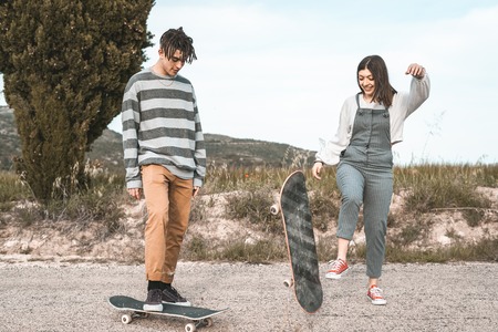 Young couple riding a skateboard on a road. Concept of millenials Skateboarders on skates