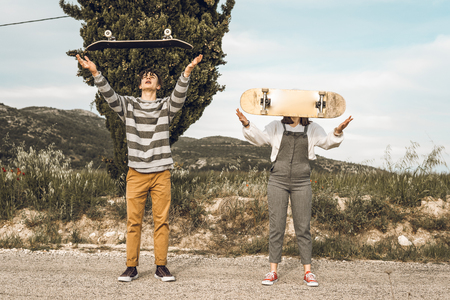 Trendy young couple having fun with a skateboard on the road. Photo style social networksの写真素材