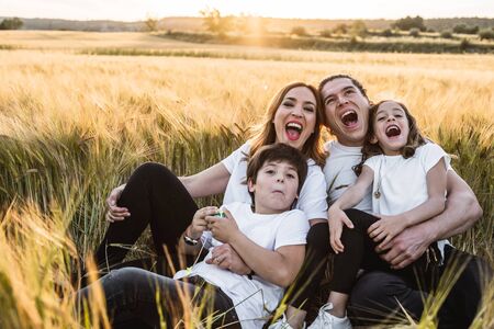 Funny happy family smiling in the field with a sunsetの写真素材
