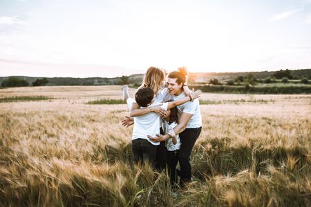 Happy family hugging in the field and smiling at a sunset.の写真素材