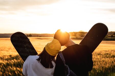Fashion Lifestyle, Happy casual young couple with skateboard, backlit at sunsetの写真素材