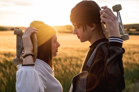 Fashion Lifestyle, Happy casual young couple with skateboard, backlit at sunsetの写真素材