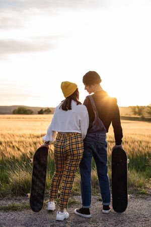 Fashion Lifestyle, Happy casual young couple with skateboard, backlit at sunsetの写真素材