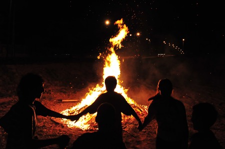 Children are holding hands and dancing in a circle around a bonfire.の写真素材