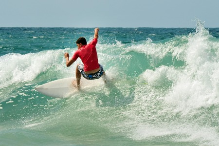 An image of a young male teenager with a red shirt riding a wave during a competition
