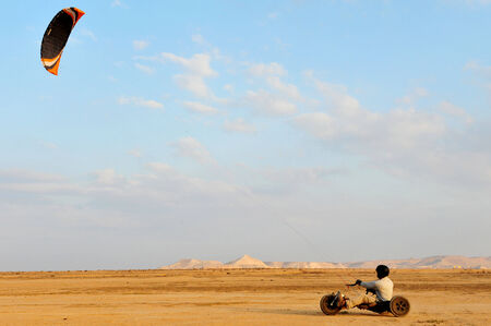 A paraglider with a trike buggy is paragliding over the desert against a clear blue sky.