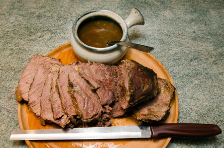 Cooked Roast beef on a cutting meat wooden board with roast beef slicing knife and gravy bowl.の写真素材