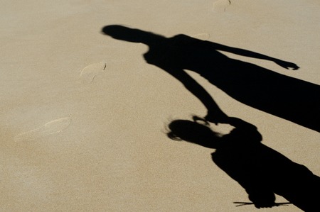 Shadow of mother and her child over a sand on the beach during summer vaction.の写真素材