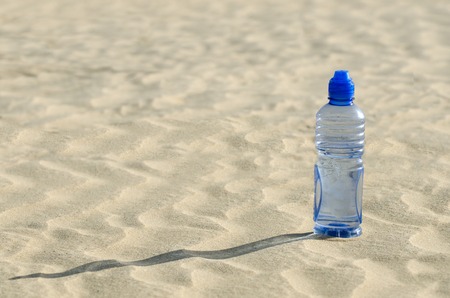A cold bottle of water sitting in a sand dune in the desert.の写真素材