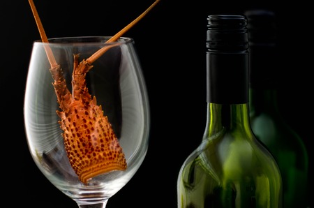 Two bottles of wine and a wine glass with a crayfish had inside it on black background.の写真素材