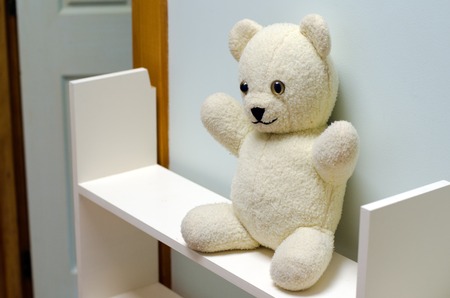 Sad white teddy bear on a self outside a children room at home.の写真素材