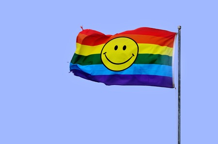 Rainbow flag with smiley face wave in the wind on blue skyの写真素材