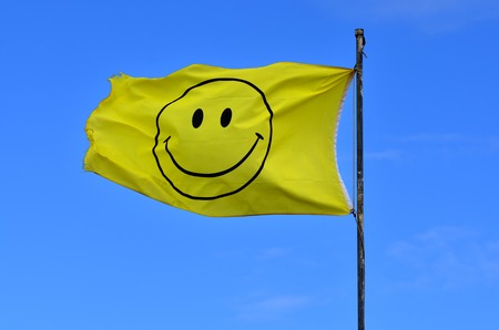 Yellow flag with smiley face wave in the wind on blue sky