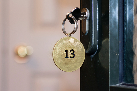 Closeup of an old keyhole of room number 13 with key on a wooden antique door.の写真素材
