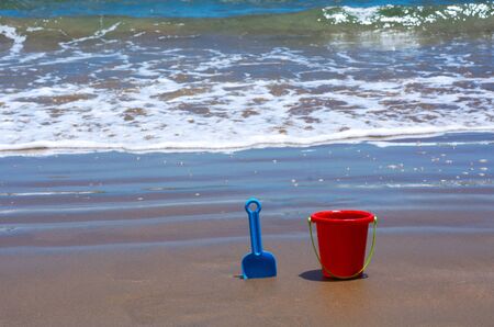 Children's beach toys on seaside.Red bucket and blue spade on sand with the sea in the background on sunny day.の写真素材