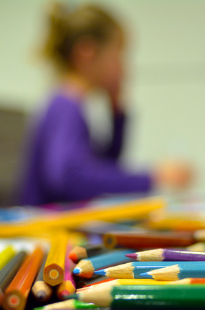 Selective focus of colour pencils in the foreground while a child, girl age 05,  thinking about art in the background. Vertical (copy space)の写真素材