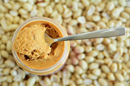 Crunchy peanut butter in jar with spoon with  dry roasted peanuts in the background. Concept photo of foodの写真素材