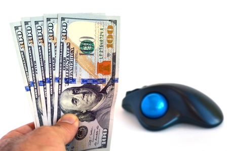 Mans hand holds one hundred (100) US Dollars banknotes against computer mouse isolated on white background. Money Concept of online internet banking, trade and credit.の写真素材