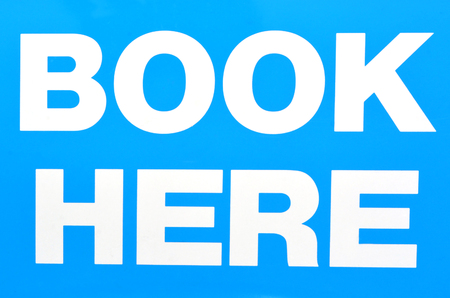 White sign of Book Here isolated on light blue background.Concept photo of travel , tourism, vacations , destinations, attractionsの写真素材