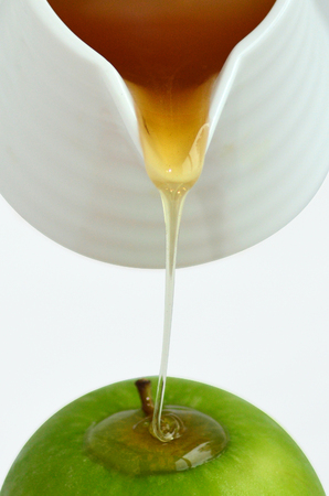 Fresh honey drop from honey pot on green apple during Rosh Hashanah Jewish holiday, on white background with copy spaceの写真素材