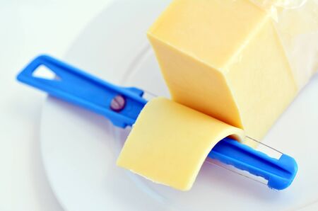 Yellow cheese slice and Cheese slicer on a white plate isolated on white background. Food conceptの写真素材