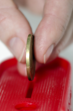 A hand places a gold coin into red donation, savings or tip boxの写真素材