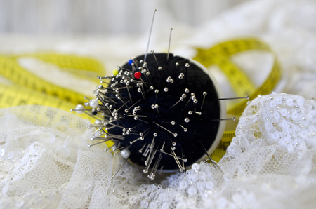 Wedding dress fabric, measure tape and cushion with sewing pins on tailor working table.の写真素材