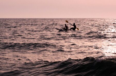 Two people raws a canoe over the ocean at sunset