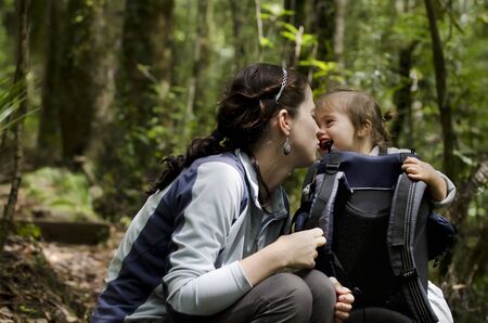 A mother and her baby backpacking through a forest, show their love for one another while they stop for a rest.の写真素材