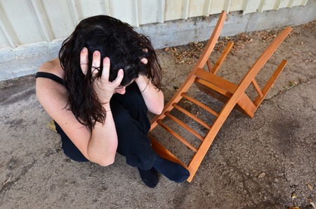 A sad woman is sitting alone on the cold concrete behind a shedの写真素材