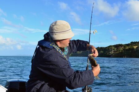 A man holds a fish that he caught during fishing at sea on a fishing boat.の写真素材