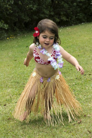 Little girl with Hawaiian Costume  of hula dancer, Hula girl dancing outdoor in the garden over green grass barefoot.の写真素材