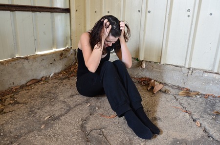 A sad woman is sitting alone on the cold concrete behind a shedの写真素材