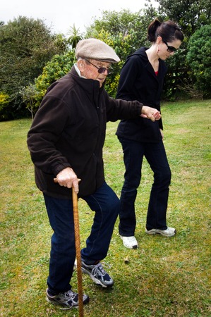 Young woman helping and supporting her grandfather to walk outdoor in the garden with his support walking stick.の写真素材