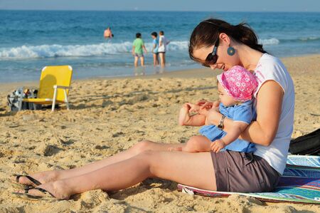 A child and her mother play in the sand together on the beachの写真素材
