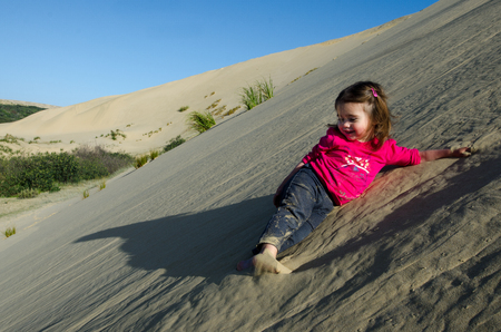 Little girl rolled down the slope of snow-white Te Paki sand dunes in Northland New Zealand.の写真素材