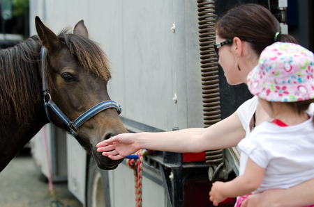 Young mother and her baby girl are petting a Rodeo show horse.の写真素材
