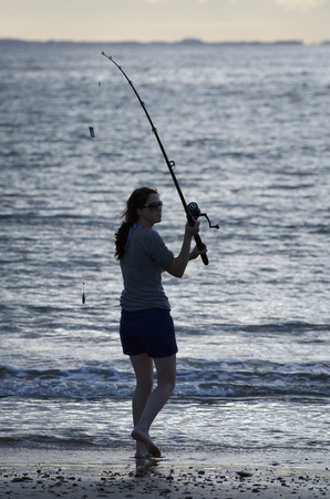 Young woman fishing at the beach during sunset.の写真素材