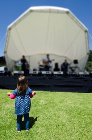 A little girl dances by herself under a stage with a band in an outdoor music concert.の写真素材