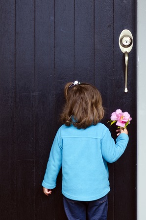 Little girl with a gift flower knocks on a house door.の写真素材