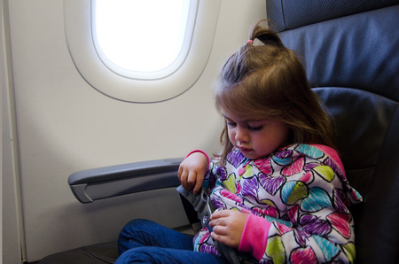 Young girl fasten seat belt on board of a airplane during air travel. (MR)の写真素材