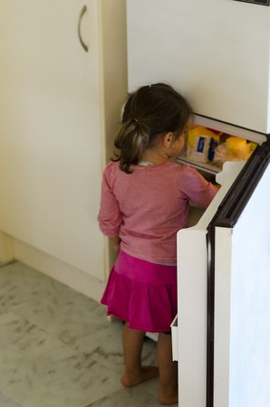 Hungry Poor little girl look for food in empty fridge at home.の写真素材