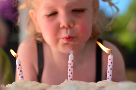 Little girl blows birthday candles during here third birthday party. (age 3)の写真素材