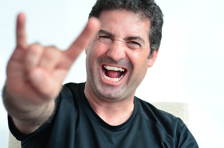 Mature man showing the devil thorns gesture sign.close up on white background.real people.Concept photo of rock and roll music fan,rudeness, aggressiveness, anger, evil, provocation, hostility.の写真素材