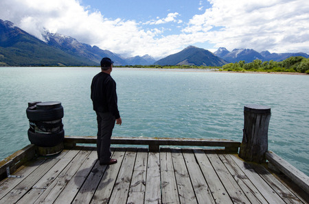 Man looks at dramatic mountains landscape from Glenorchy wharf, lake wakatipu New Zealand.の写真素材