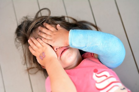Abused little girl with a broken arm covering here face while crying. Concept photo of child abuse, violent in the family,domestic violent, social issues.の写真素材