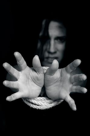Missing kidnapped, abused, hostage, victim woman with hands tied up with rope in emotional stress and pain, afraid, restricted, trapped, call for help, struggle, terrified, locked in a cage cell.の写真素材
